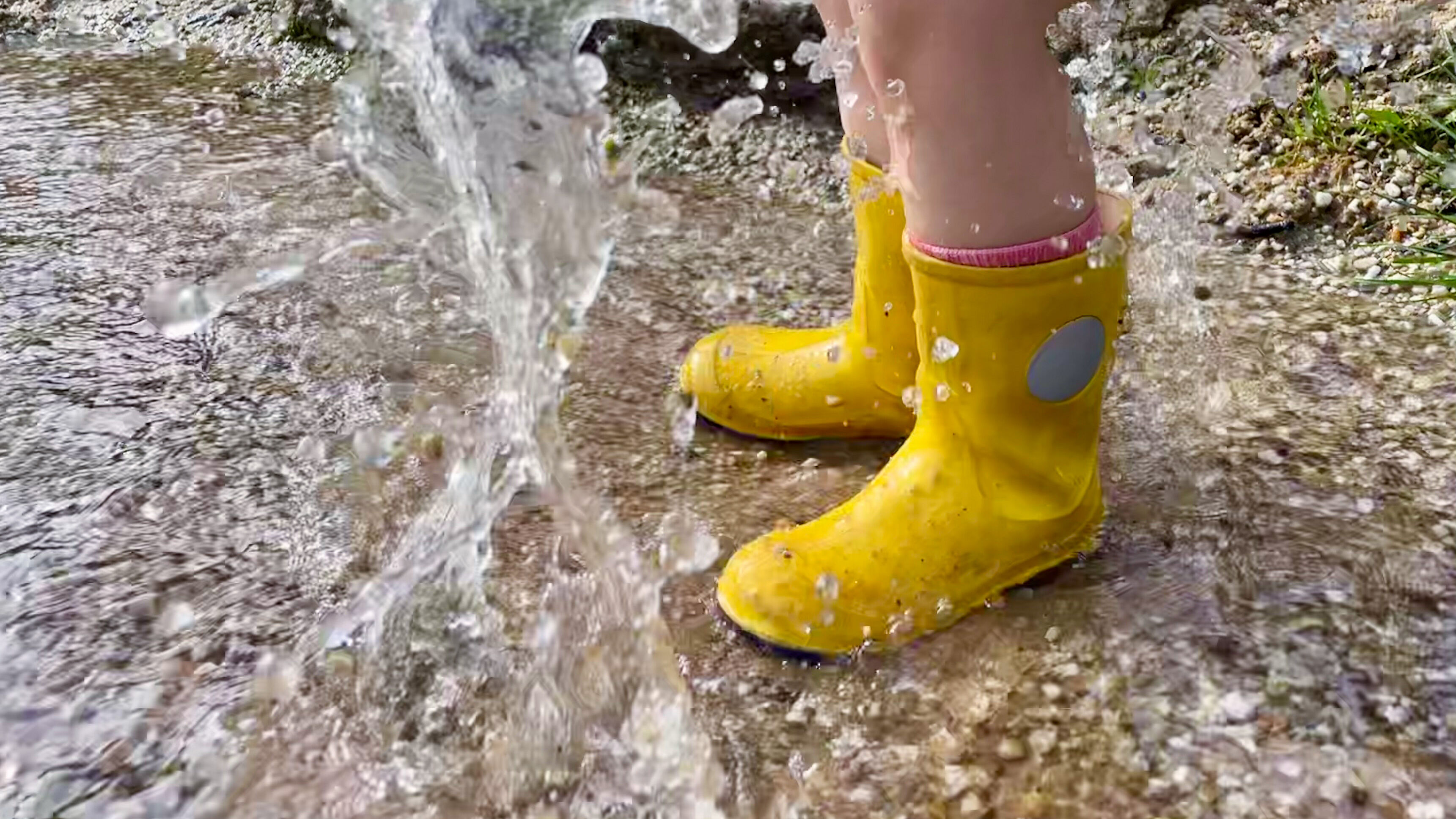 Gelbe Kindergummistiefel hüpfen in Wasserpfütze. 